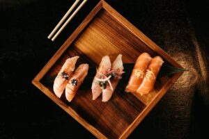 A wooden plate with premium sushi, including salmon nigiri and garnished sashimi, elegantly presented with chopsticks.