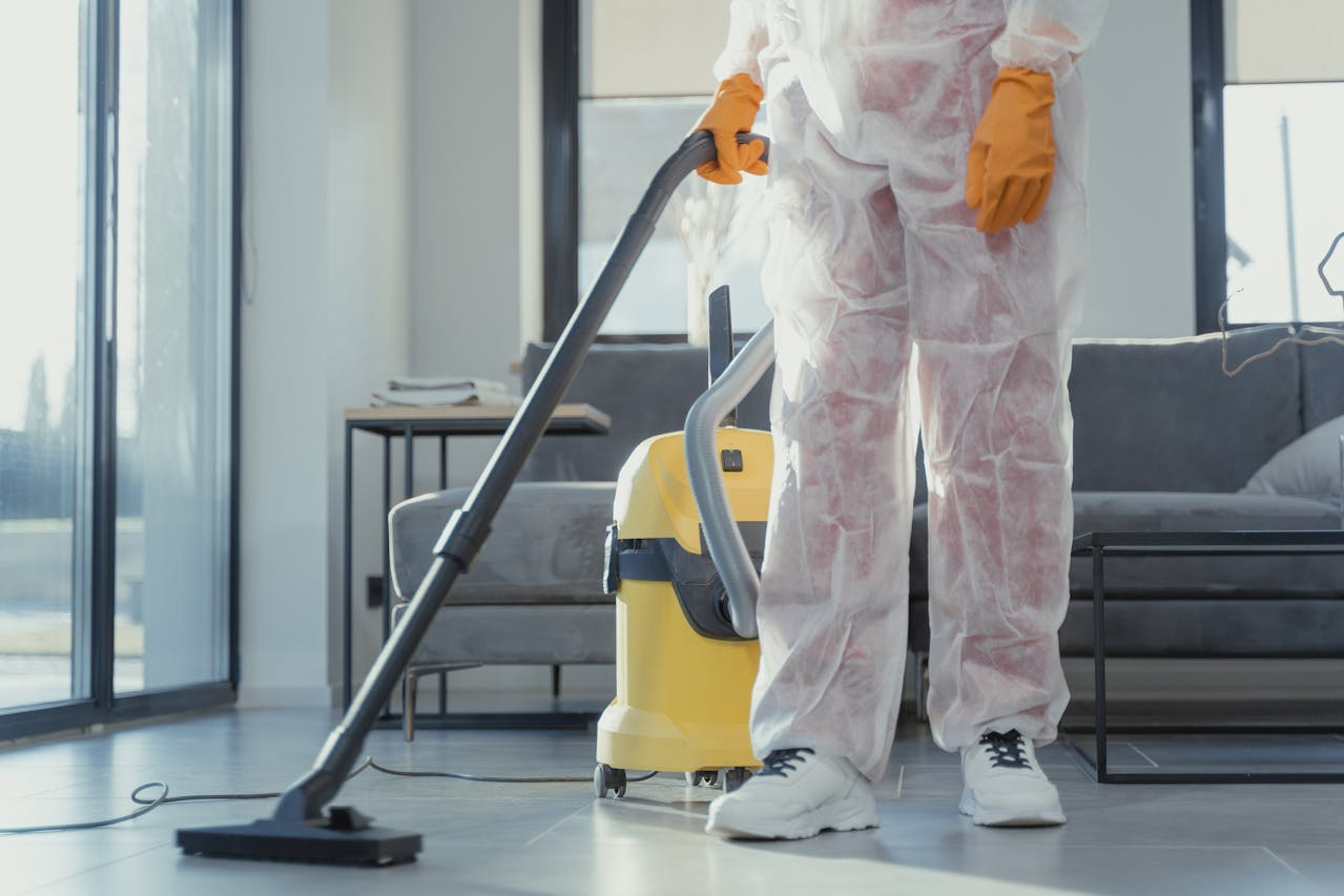 A professional cleaner in protective gear vacuuming a modern living space with a yellow industrial vacuum cleaner.